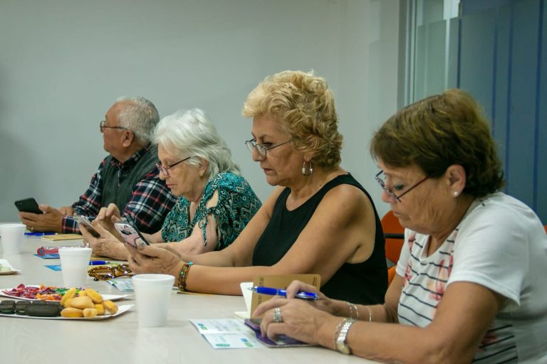 Adultos mayores reunidos en una mesa con dulces revisando sus celulares